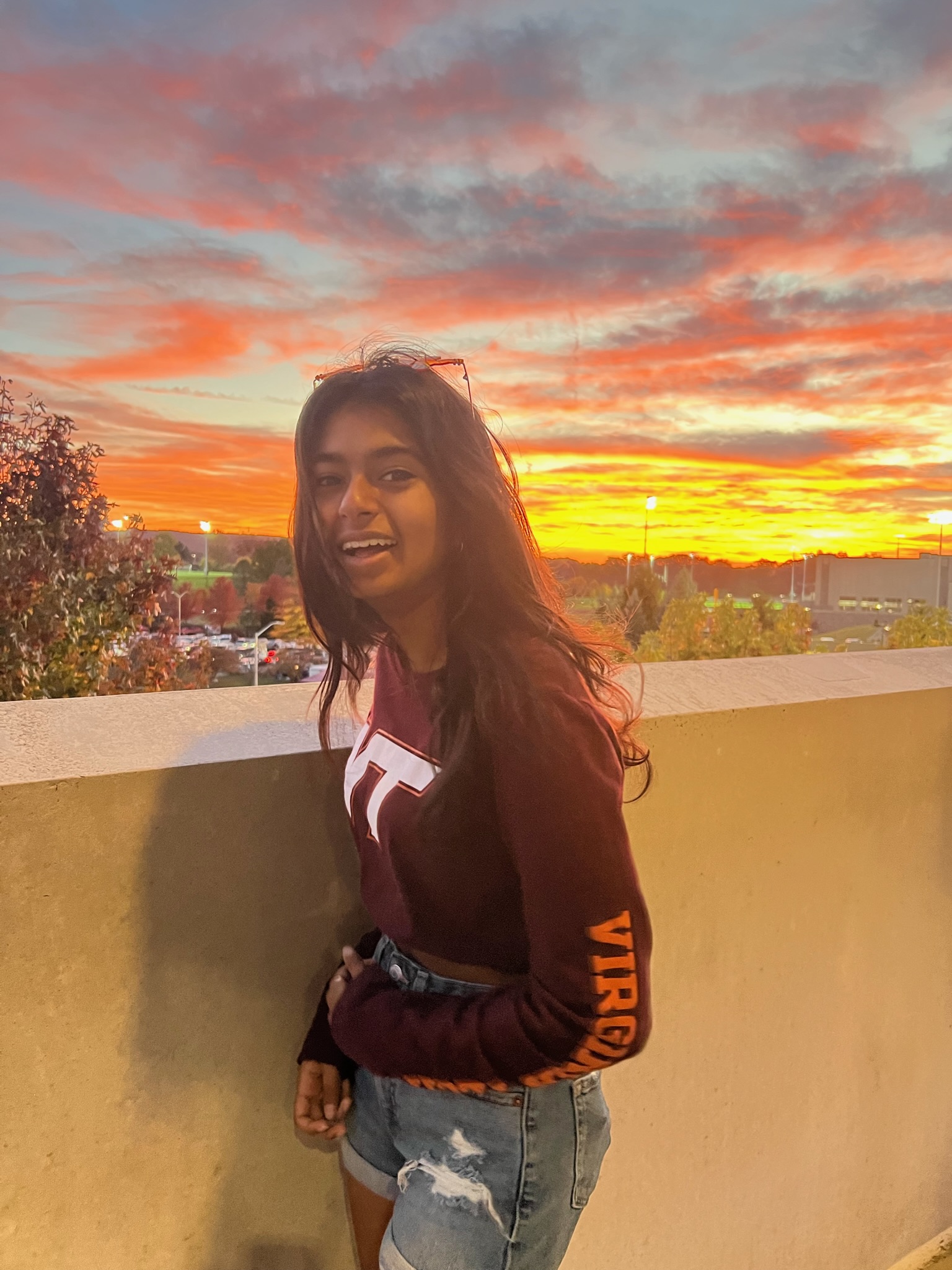 a picture of Reena Vasudevan, Reena Vasudevan, writing coach at Virginia Tech University, standing at a balcony with sunset in the background